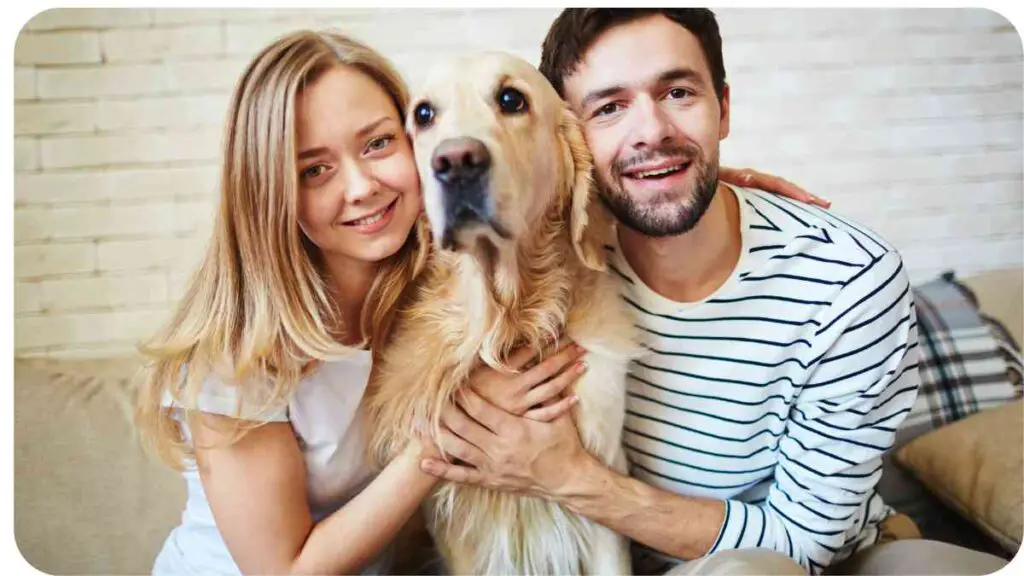 Two people are sitting on a couch with a golden retriever